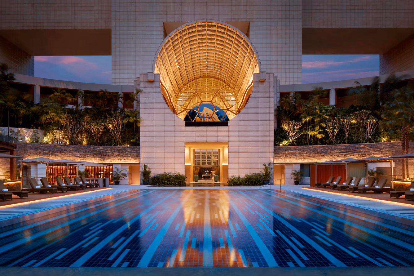 The iconic outdoor swimming pool at The Ritz-Carlton, Millenia Singapore, framed by lush tropical hotel gardens and the striking Marina Bay city skyline.