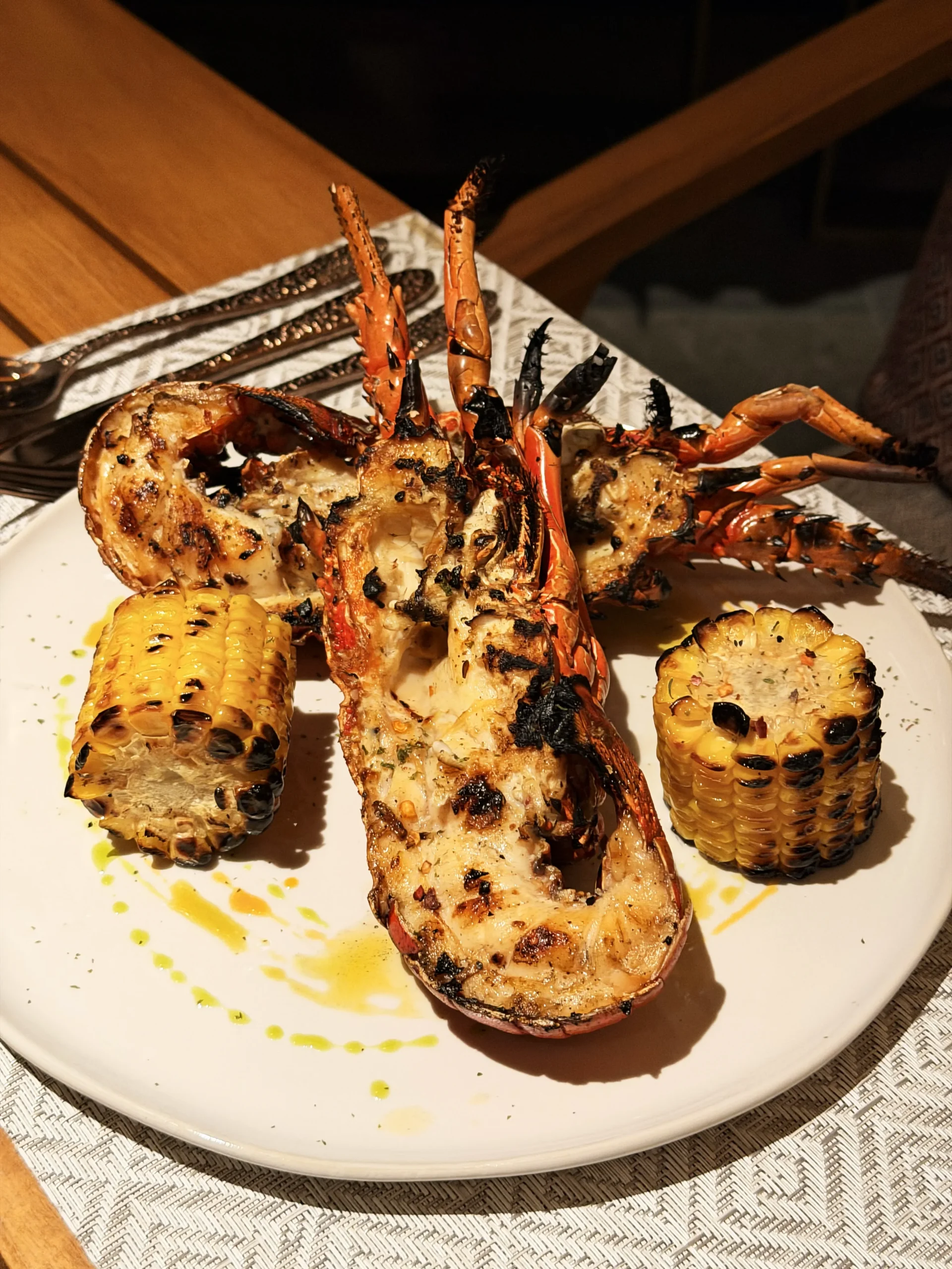 Whole grilled Flores Lobster prepared with rich compound butter, accompanied by sweet corn on the cob and a fresh petite salad at Leros, Ta'aktana Resort.