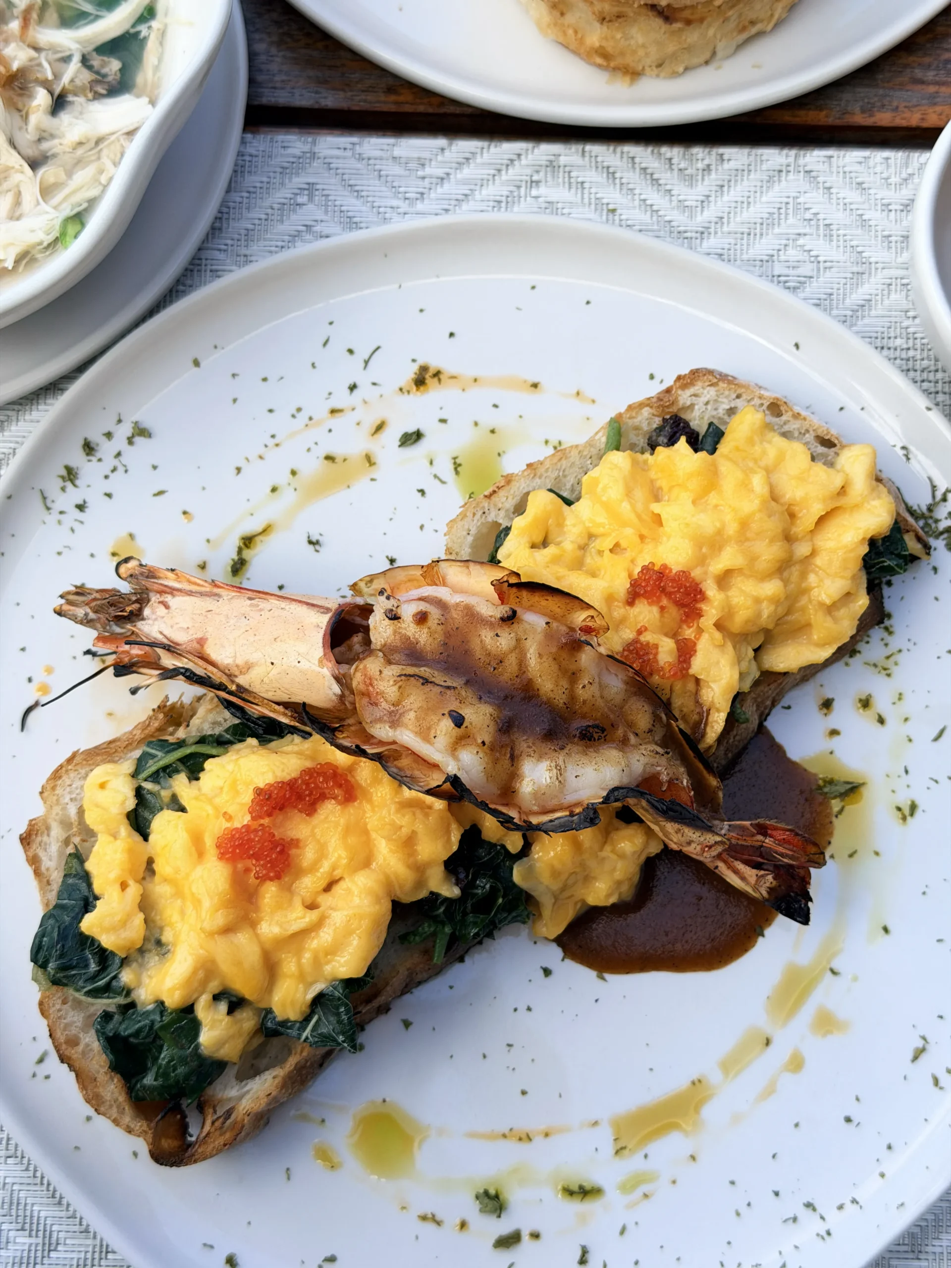 Close-up of a breakfast plate featuring creamy scrambled eggs topped with sautéed prawns, served with a side of fresh mango juice.