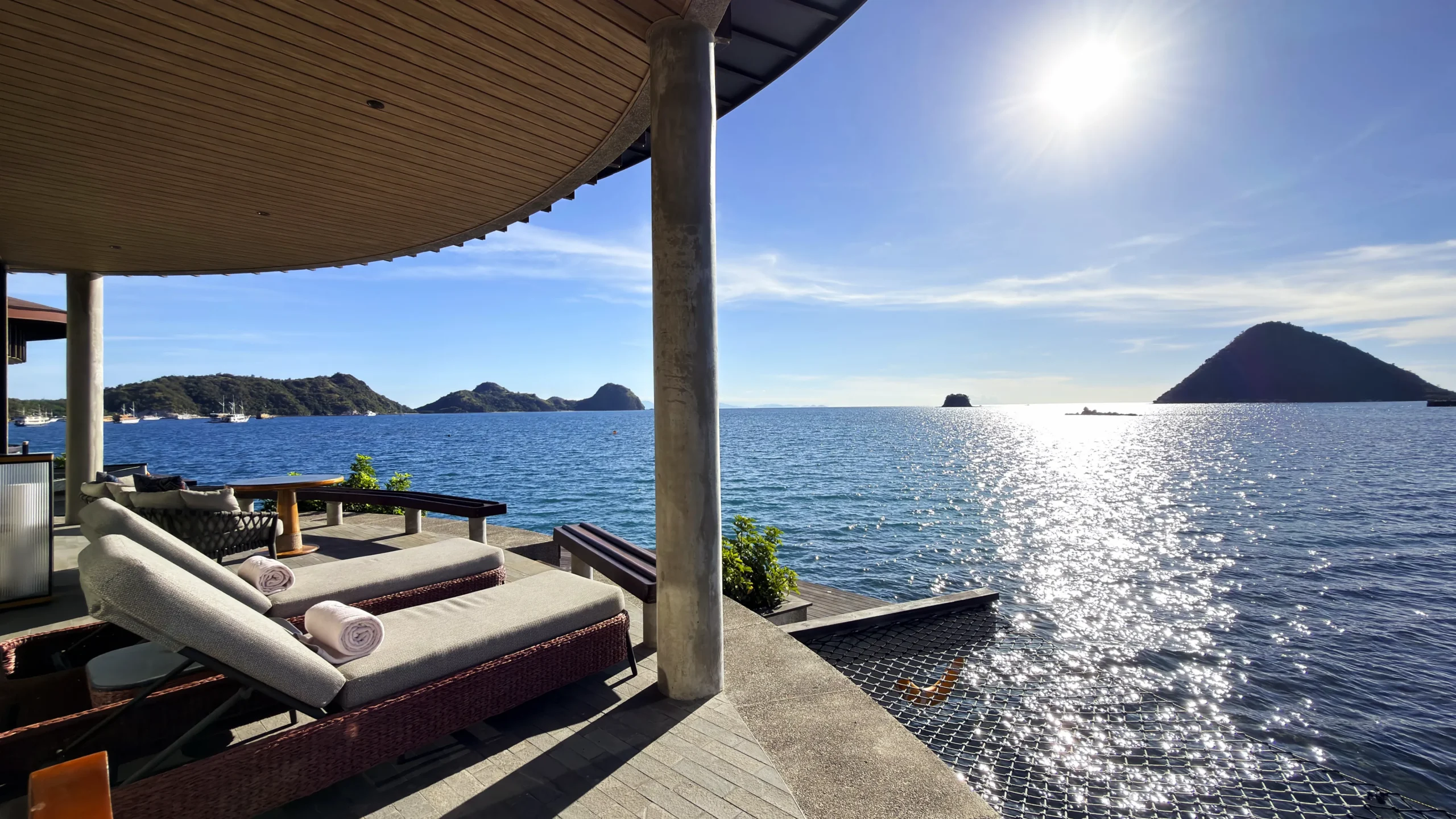Private sun deck of a Ta'aktana overwater villa, furnished with comfortable lounge chairs and direct step-down access into the calm, crystal-clear water.
