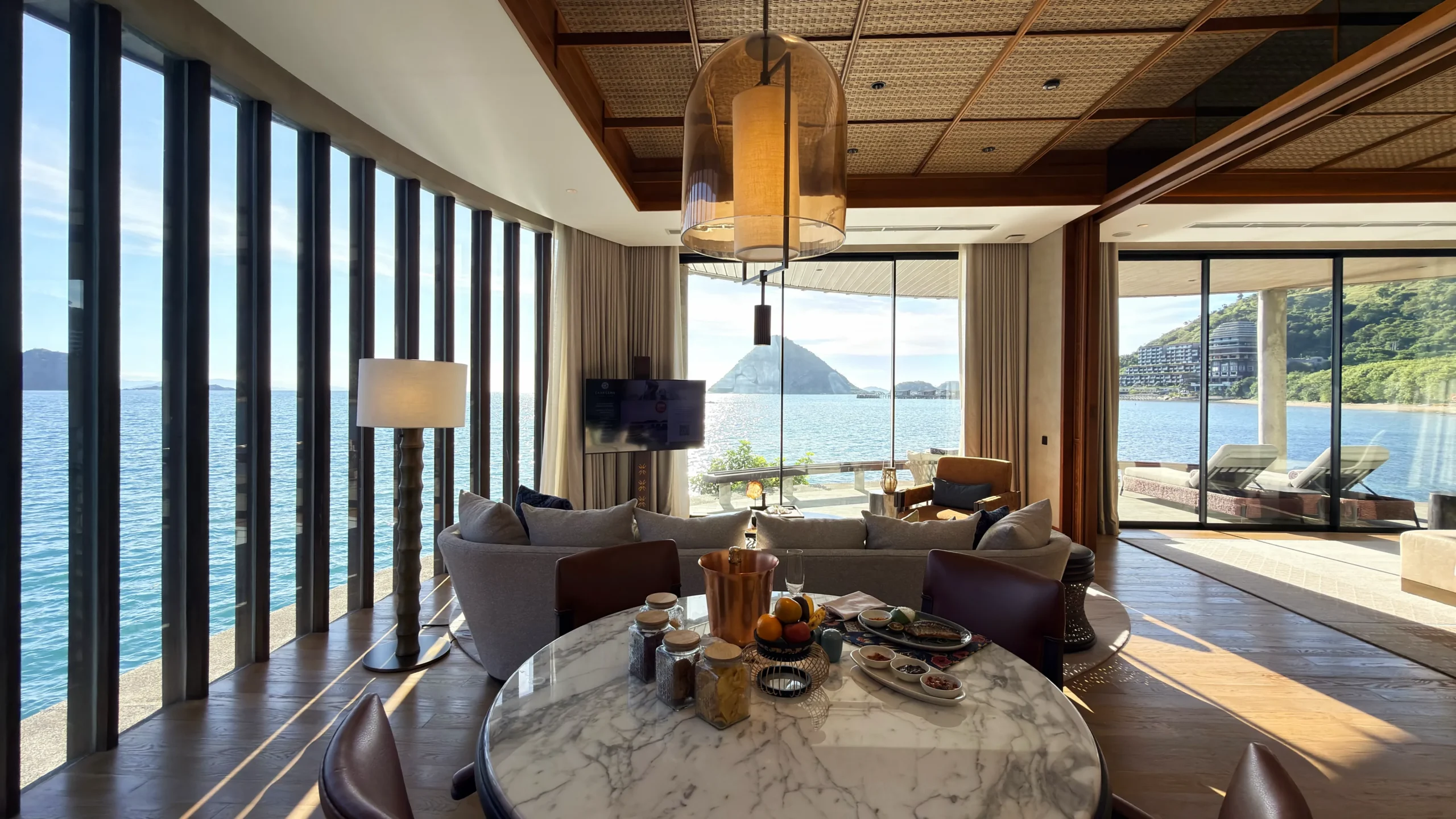Interior of a luxury overwater villa featuring phinisi boat-inspired decor, macrame headboard artwork, and floor-to-ceiling ocean views.