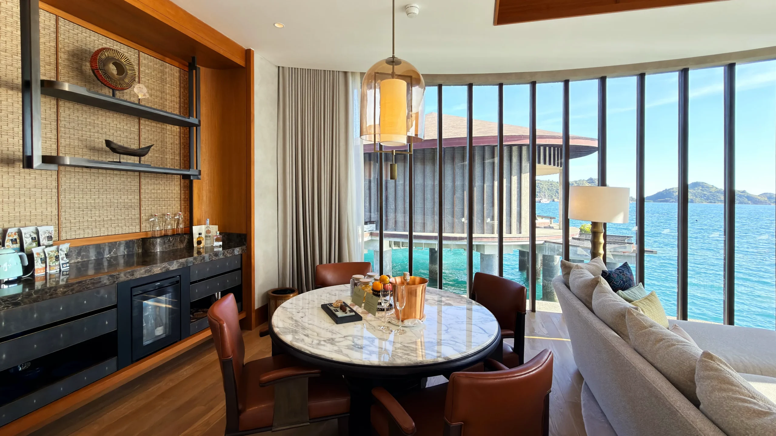 Sunlit living area inside a luxury overwater villa at Ta'aktana, featuring locally inspired decor, high ceilings, and panoramic views of the Flores Sea.