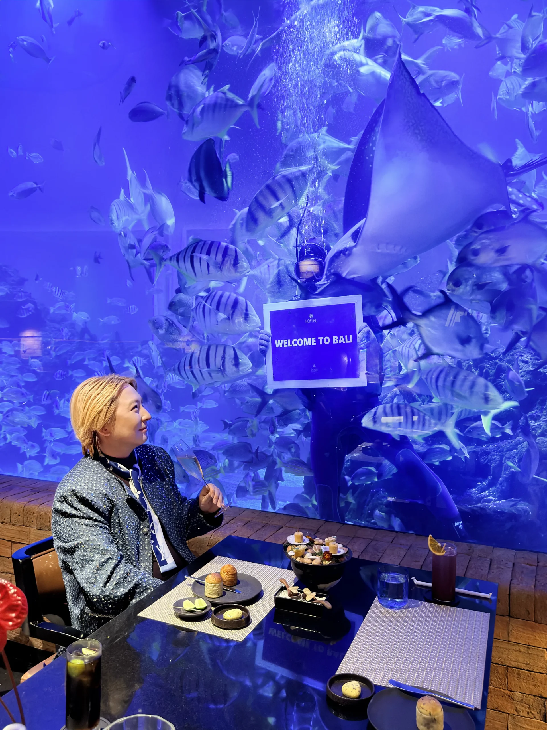 Stefano Malachi experiencing Bali's first aquarium restaurant at Koral Restaurant, surrounded by vibrant marine life inside a stunning underwater dining setting at The Apurva Kempinski Bali.