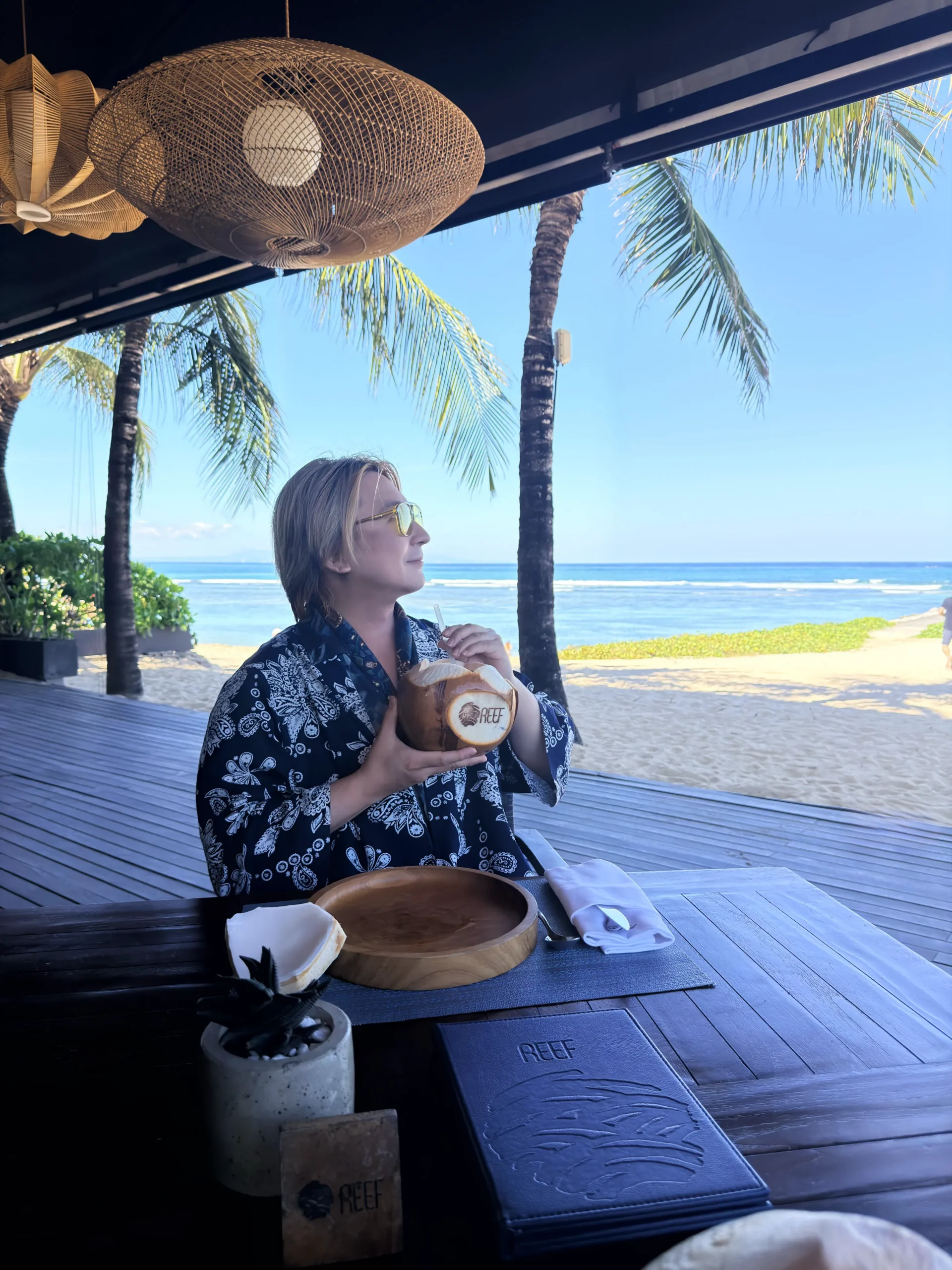 Stefano Malachi enjoying relaxed beachfront dining at Reef Beach Club, framed by the 42-metre infinity pool and tropical coastline at The Apurva Kempinski Bali.