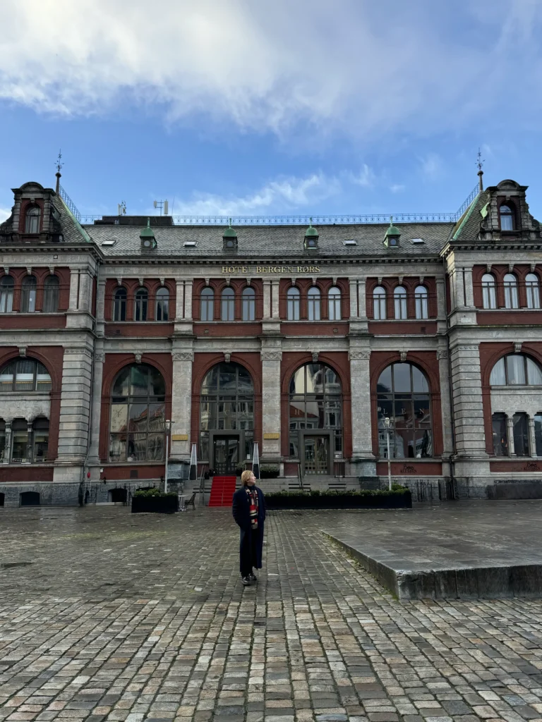 Stefano Malachi checking in at the historic Bergen Børs Hotel as warm golden hour sunset light illuminates the Neo-Renaissance architecture in the heart of Bergen, Norway.