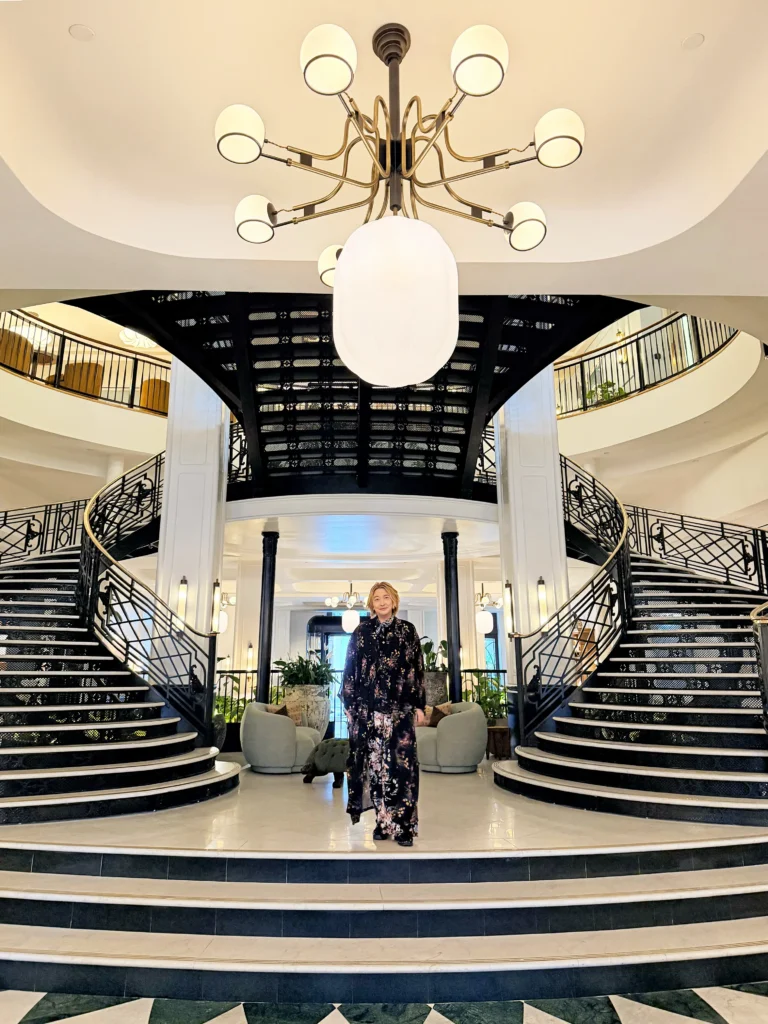 Stefano Malachi making a grand arrival on the iconic, hand-rebuilt grand staircase at Six Senses London inside The Whiteley, showcasing the historic Art Deco architecture and glass-domed ceiling.